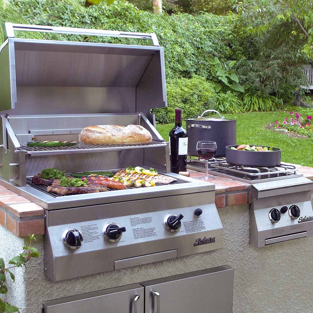 Stainless built-in gas grill outdoors with open hood, grates and controls