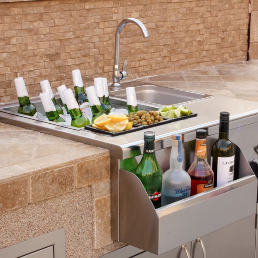 Stainless beverage prep station with open storage drawer, bottles, sink, and faucet
