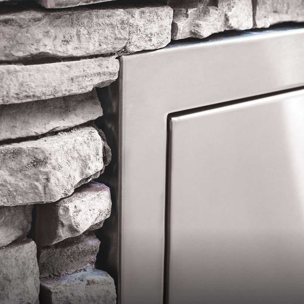 Narrow stainless trash drawer with smooth metal frame and open interior against stone masonry