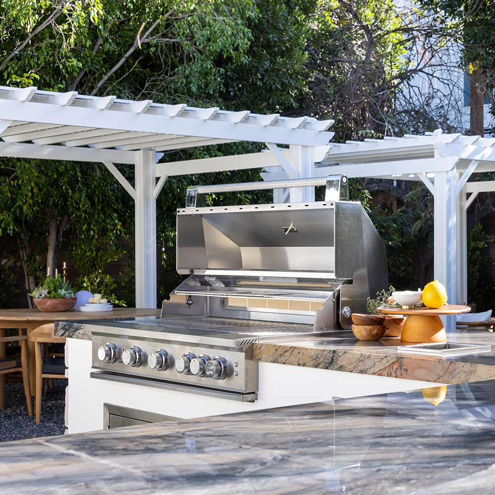 Stainless steel built-in gas grill on stone island with lid open and front burner knobs
