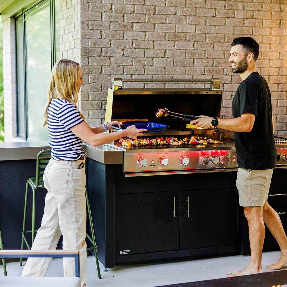 Stainless steel built-in gas grill with open hood and illuminated burners