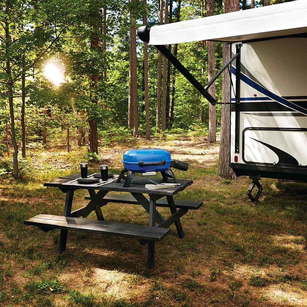 Blue portable tabletop gas grill on a wooden picnic table outdoors, lid closed