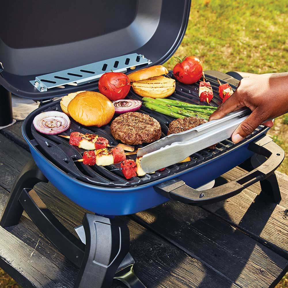 Blue portable tabletop gas grill open with burgers, vegetables, and bread on grates