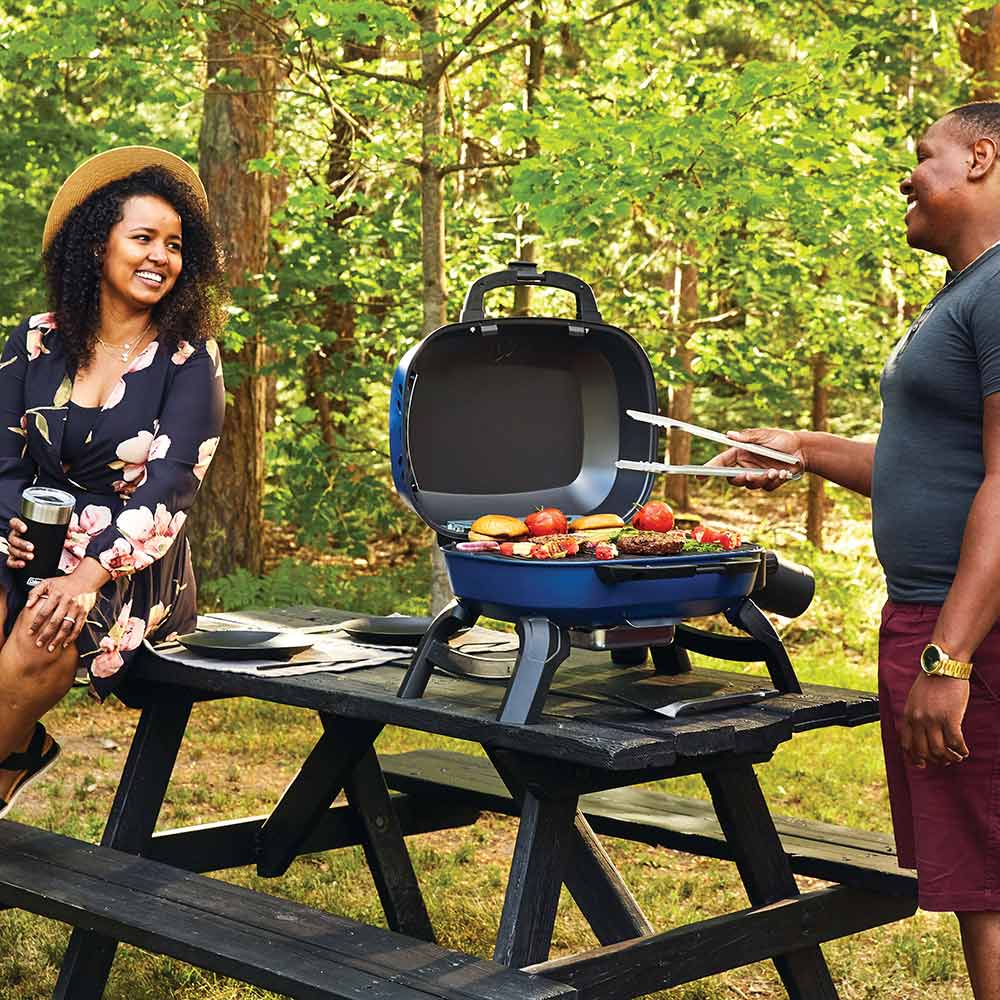 Blue portable tabletop gas grill open with mixed food on the cooking grate