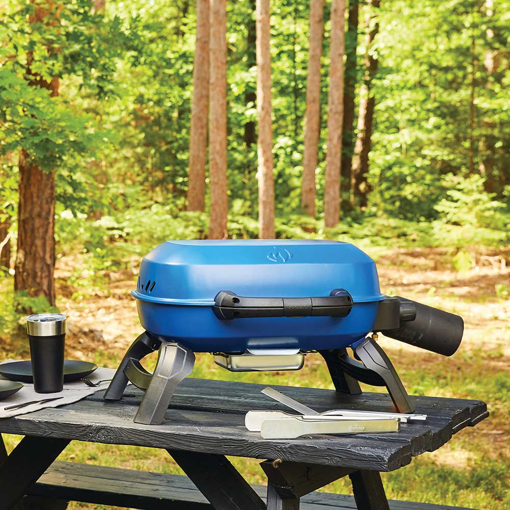 Blue portable tabletop gas grill on a wooden table outdoors, lid closed