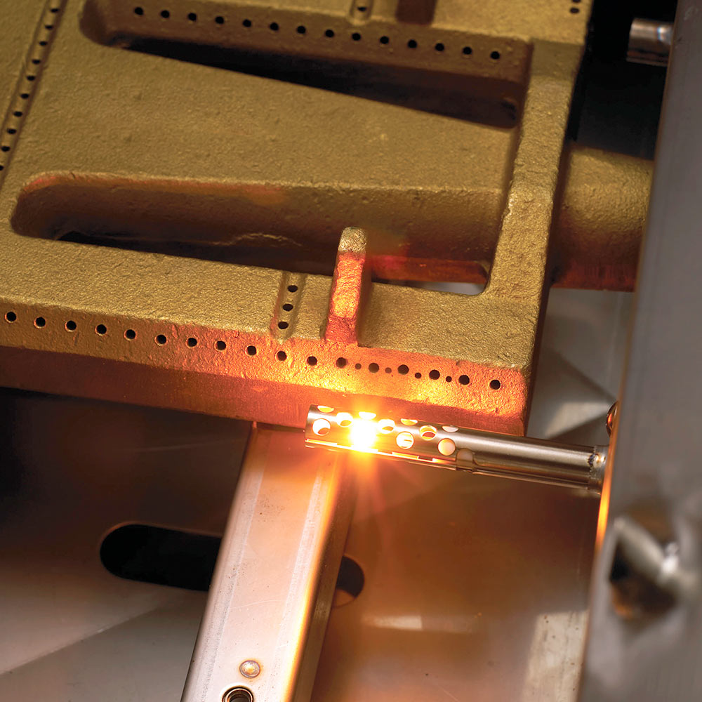 Burner ignition area with glowing flame inside stainless steel firebox