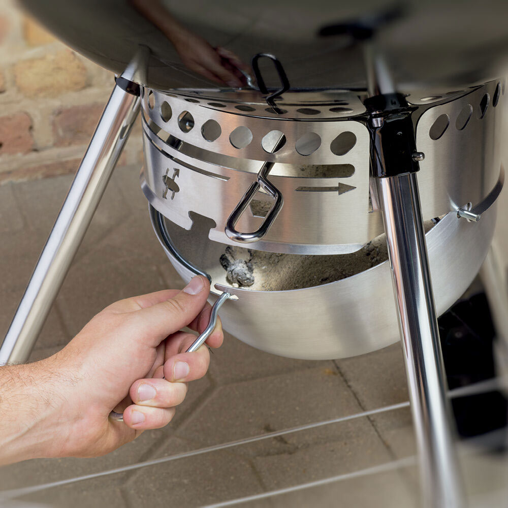 Charcoal grill bowl with ash tray and a hand adjusting the control lever