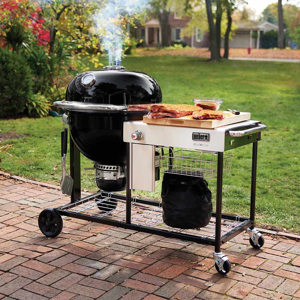Weber 24-inch charcoal grill with open lid and cooked meat on side prep surface