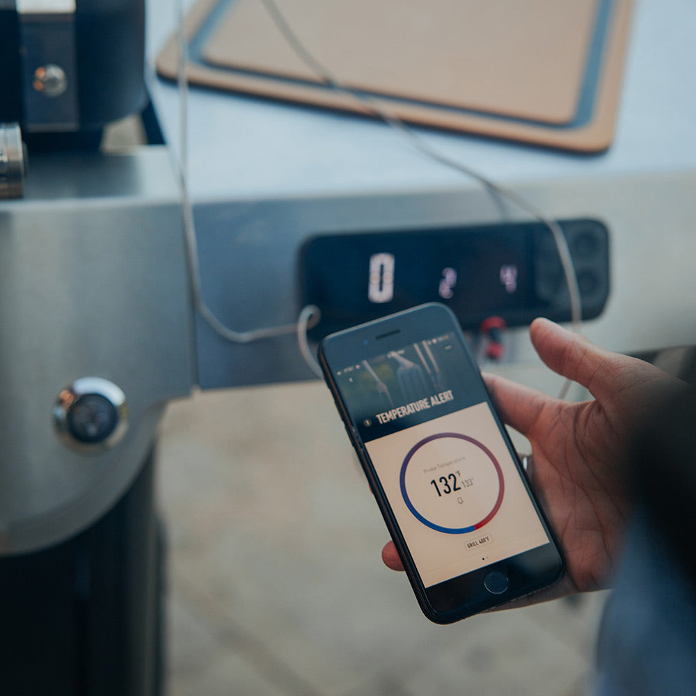 Mobile app controlling gas grill temperature on a smartphone near the grill display