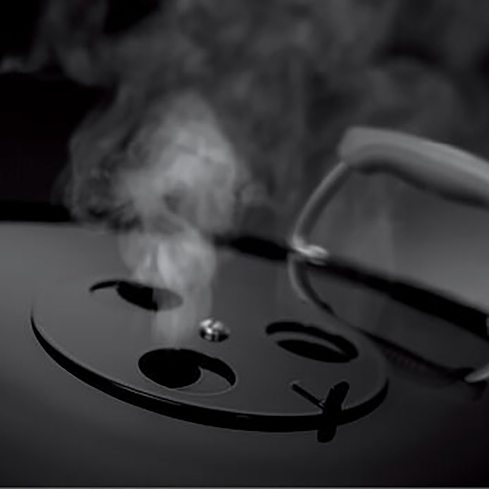 Charcoal kettle grill cooking grate with light smoke rising and heat near burners.