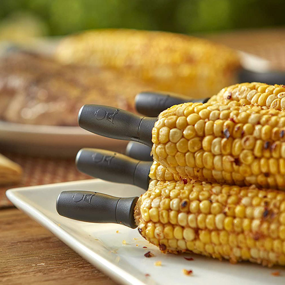Corn holder set with three black forks attached to yellow corn on a white tray