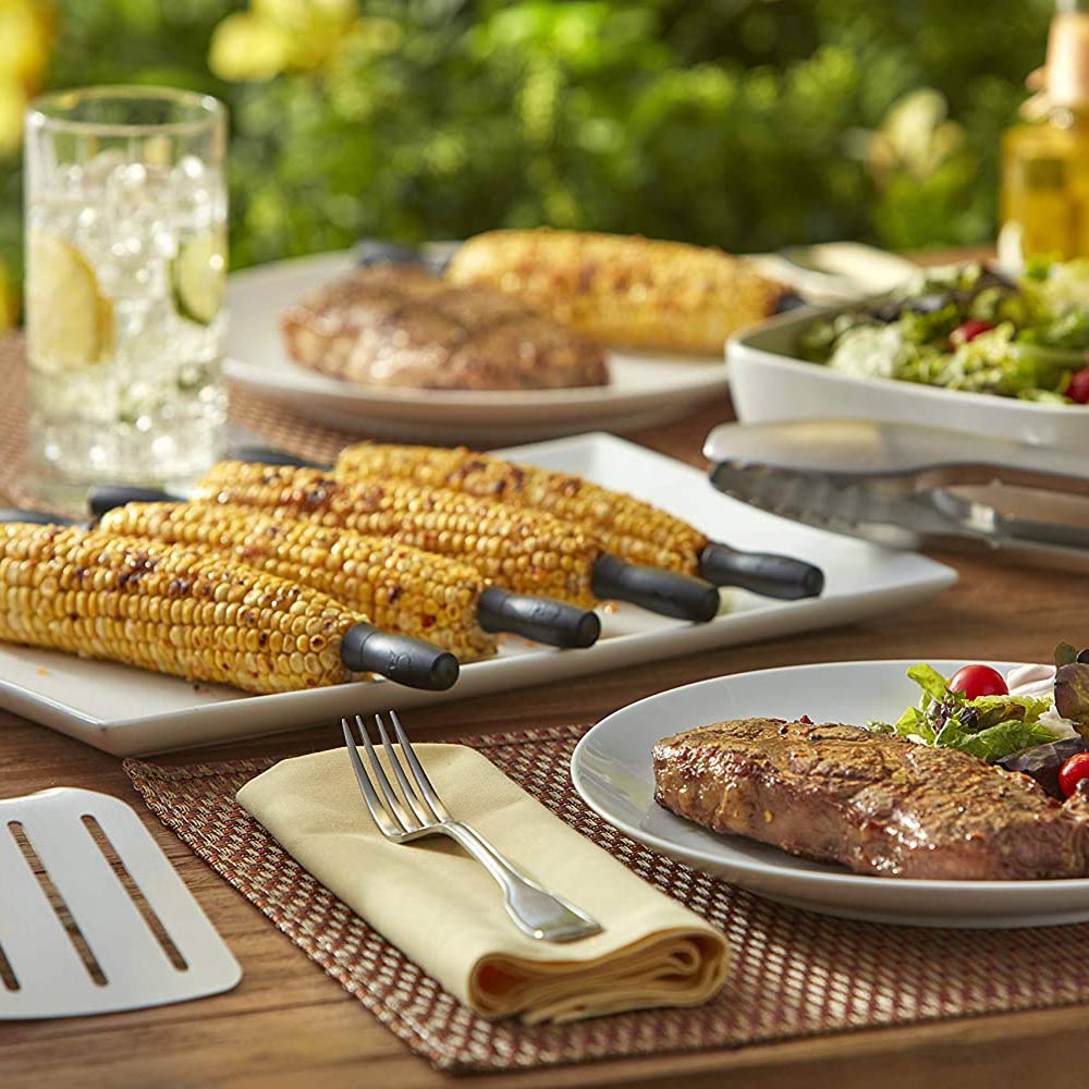 Corn holder set with black forks placed on yellow corn cobs at an outdoor table
