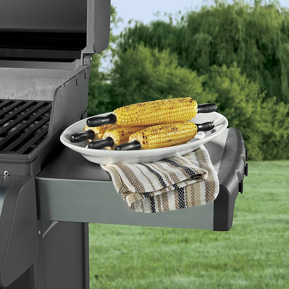 Corn holder set on a grill side tray holding two yellow corn cobs with black forks