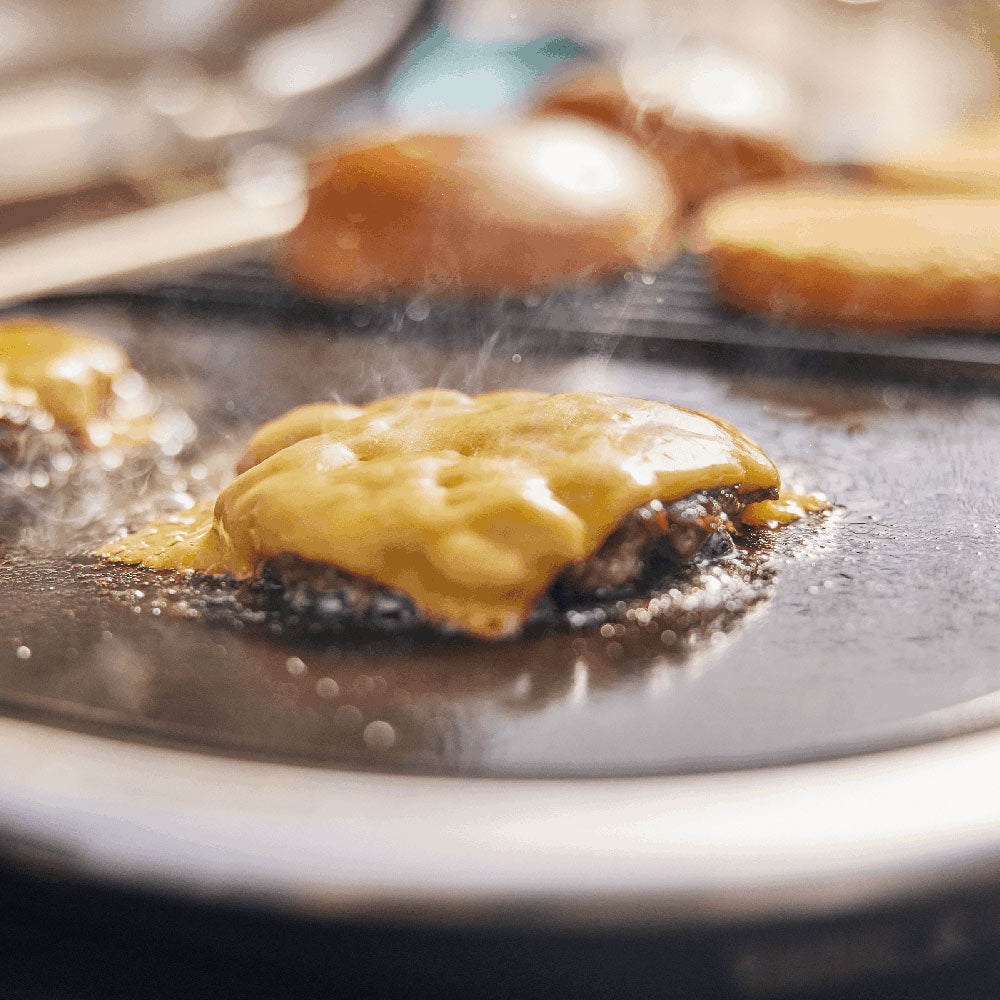 Sizzling patty on flat griddle surface with steam and browned edges