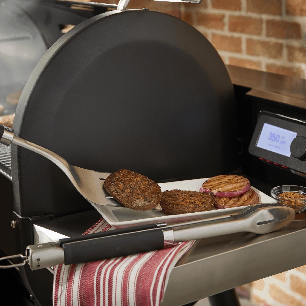 Stainless steel spatula and tongs with black handles resting on a grill