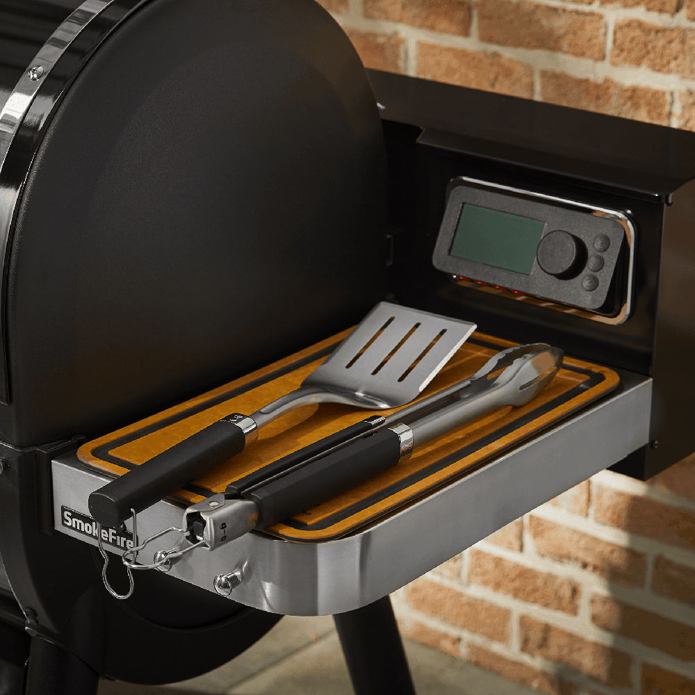 Stainless steel spatula and tongs with black handles in a grill storage tray