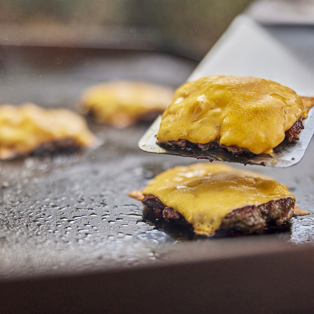 Griddle spatula lifting patties with melted cheese on hot grill