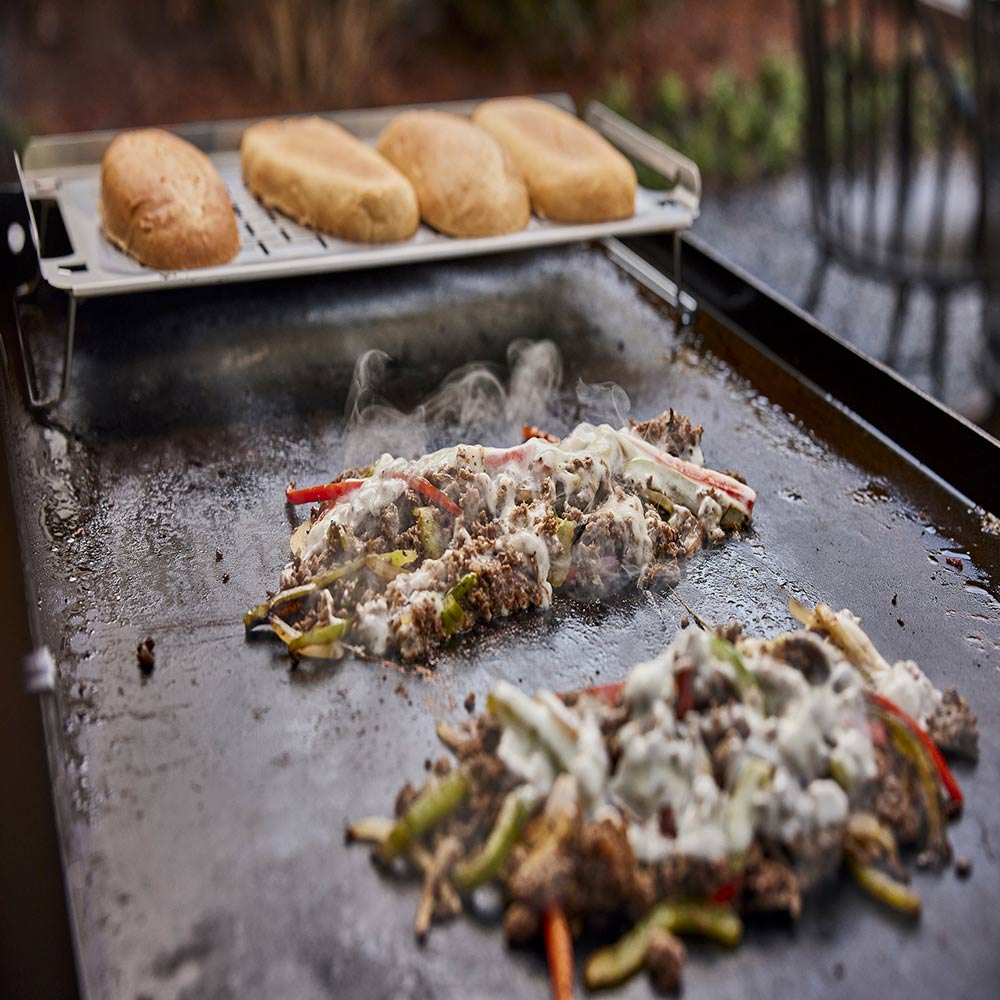 Weber griddle keep warm rack with bread rolls above grilled meat