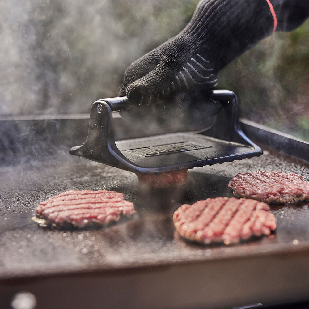 Griddle press over burgers on a hot griddle with steam rising