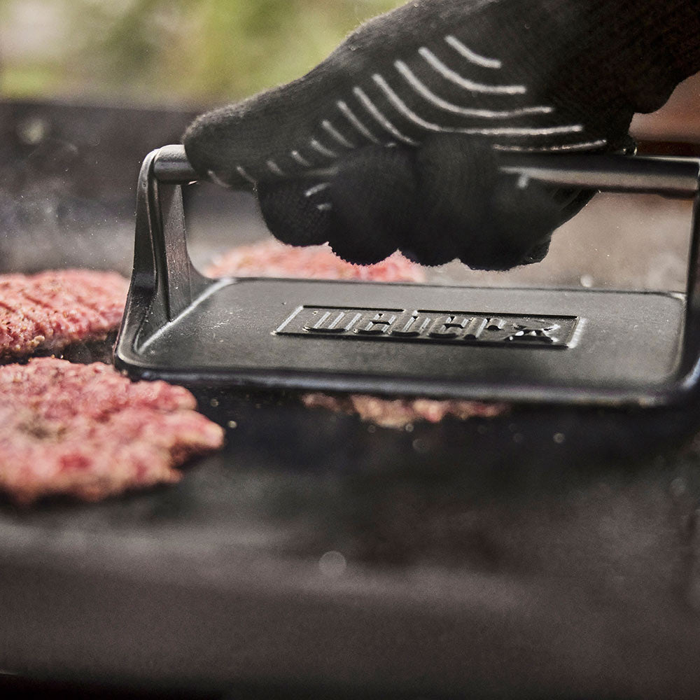 Griddle press held above burgers, ridged plate in contact