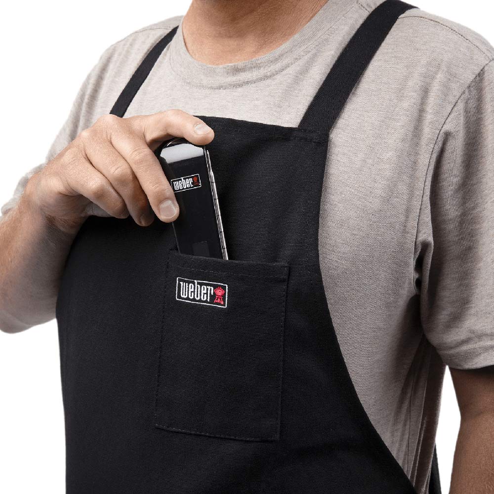 Black crossback apron with Weber logo patch and front pocket, held by strap