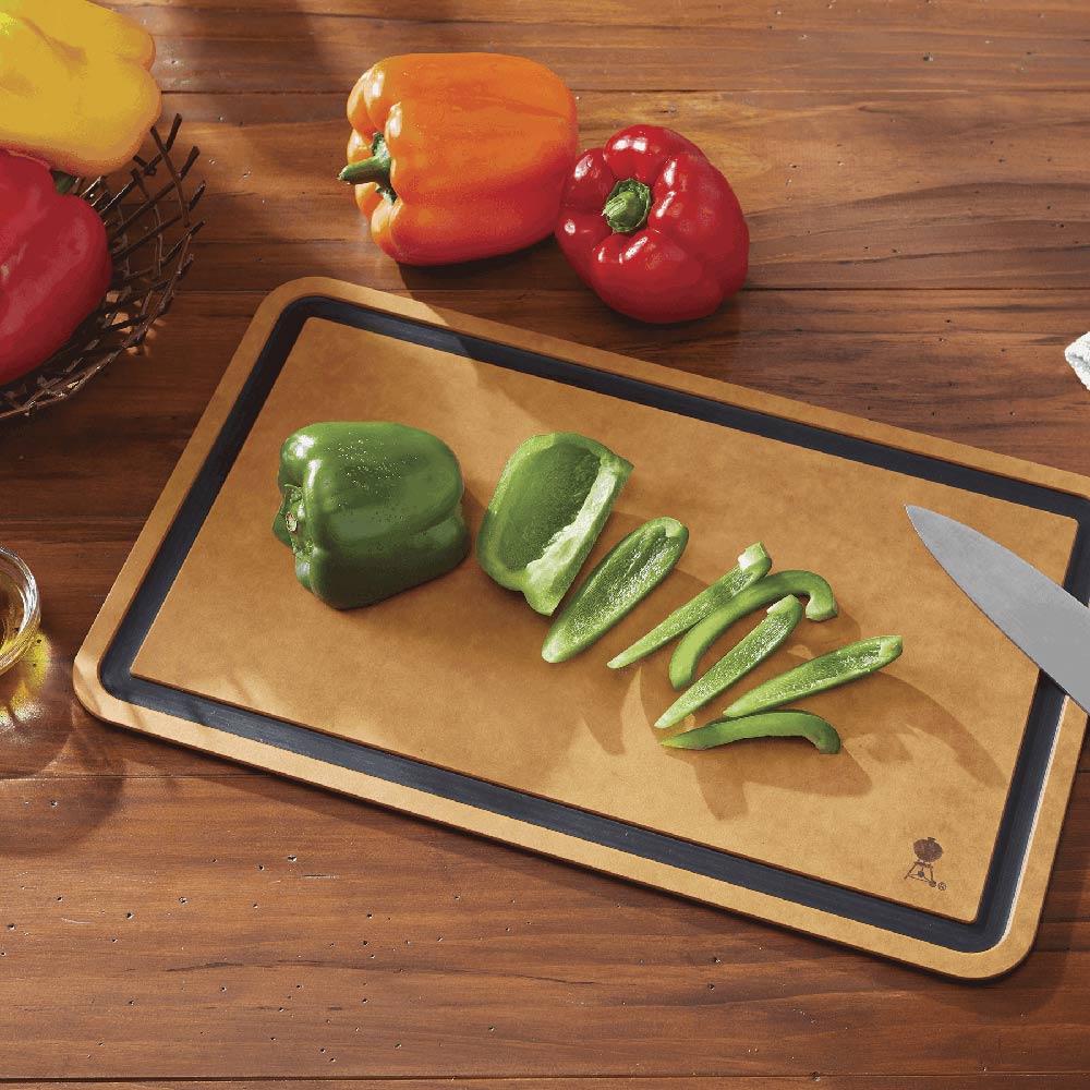 Weber cutting board with tan surface, dark border, sliced peppers and knife
