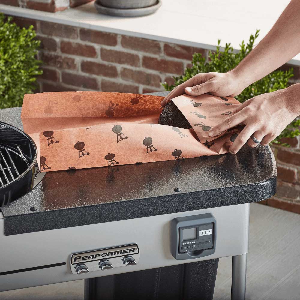Butcher paper sheet with bird pattern on a grill surface, being folded by hands