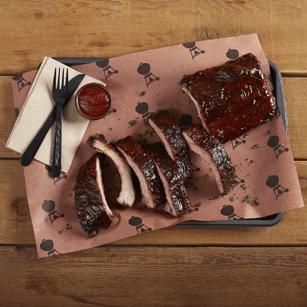 Bird-pattern butcher paper on a tray with grilled ribs, fork, and sauce