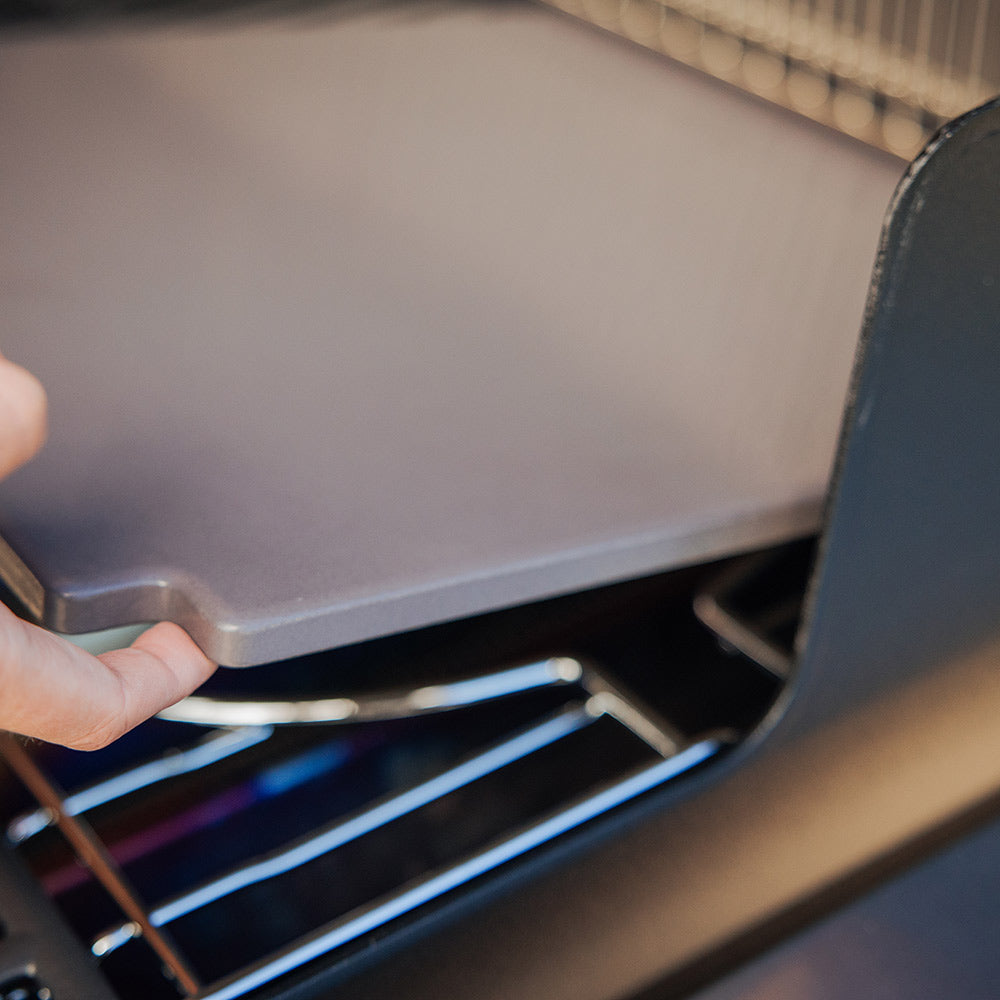 Glazed baking stone being inserted into a grill cooking area by hand