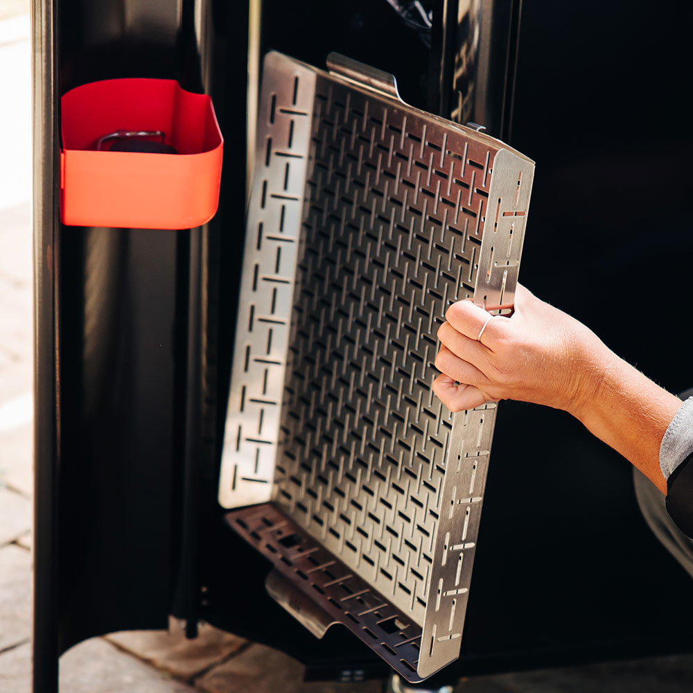Hand holding a stainless roasting basket with open grate panel inside grill