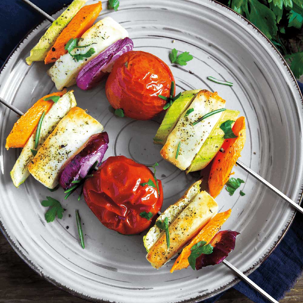 Rotisserie skewers with grilled vegetables and meat on a round metal tray, ready to serve