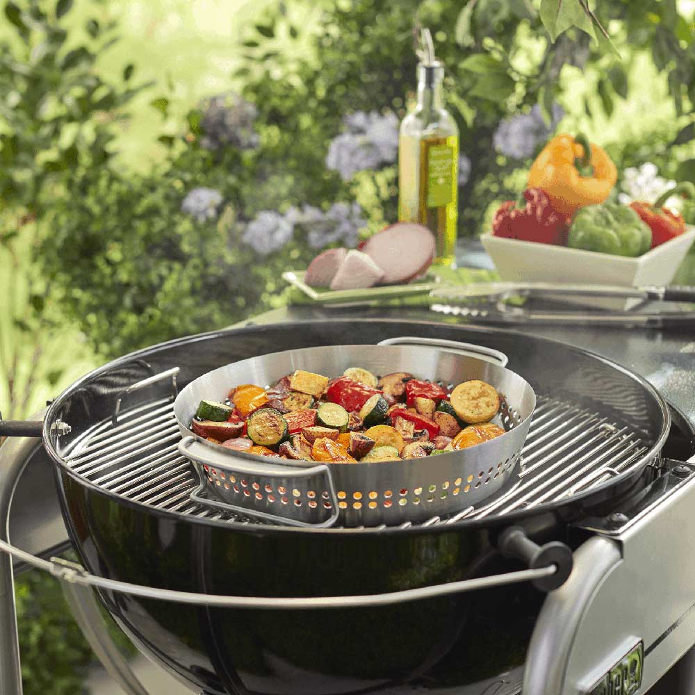 Stainless steel poultry roaster on grill with roasted vegetables and chicken