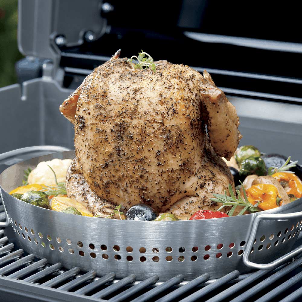 Seasoned whole chicken on stainless steel roaster basket with vegetables