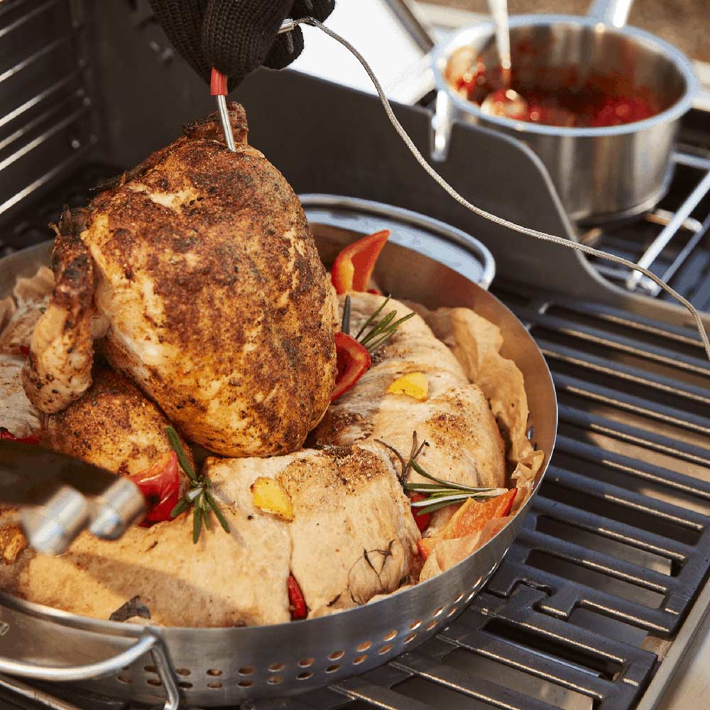 Whole chicken resting in stainless steel roaster basket on grill grates