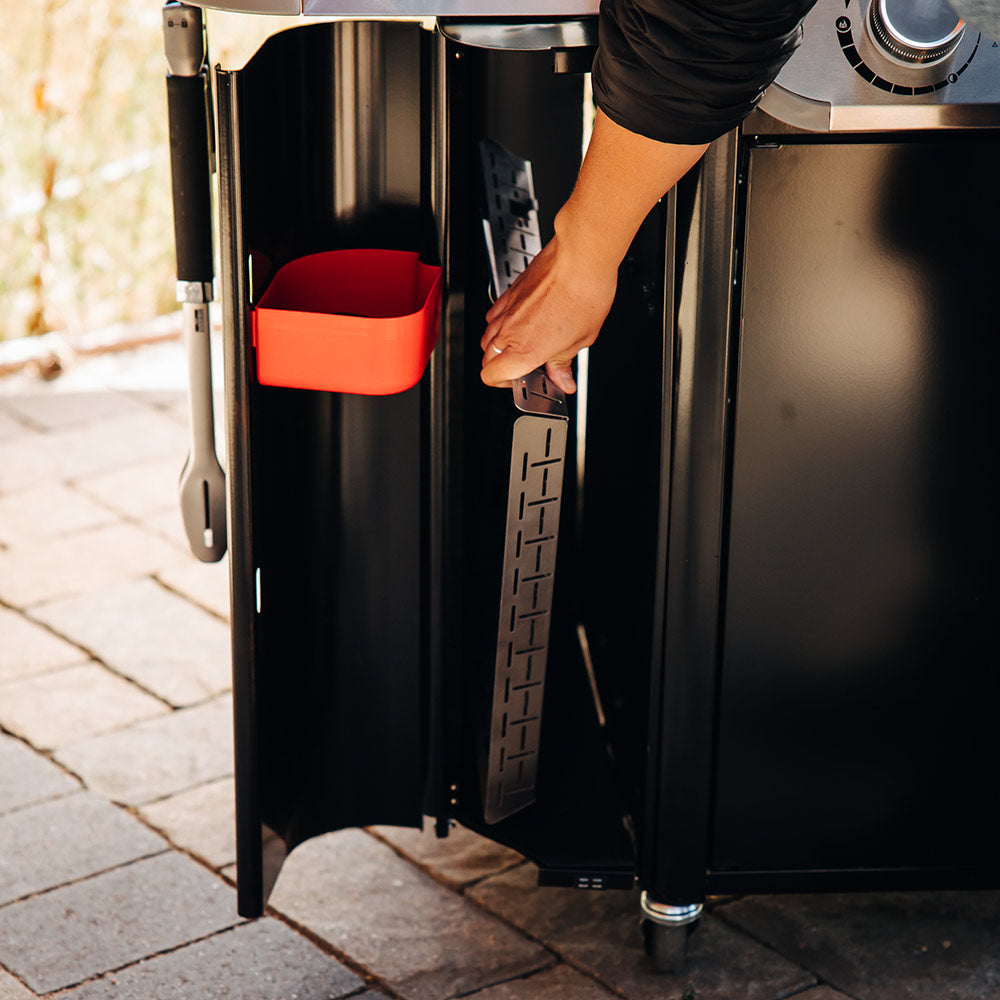 Gas grill side storage compartment open with orange interior tray and pull handle