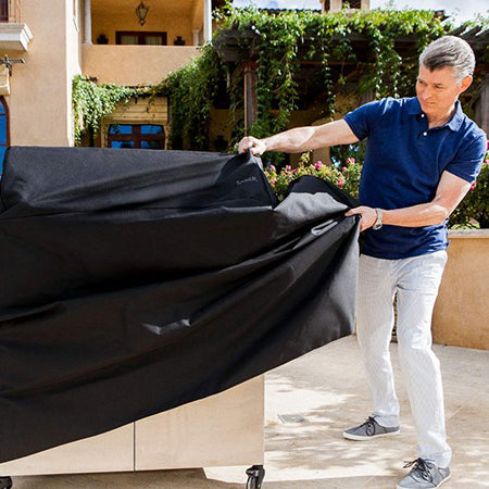 Black 4-burner freestanding grill cover being fitted on a grill with straps