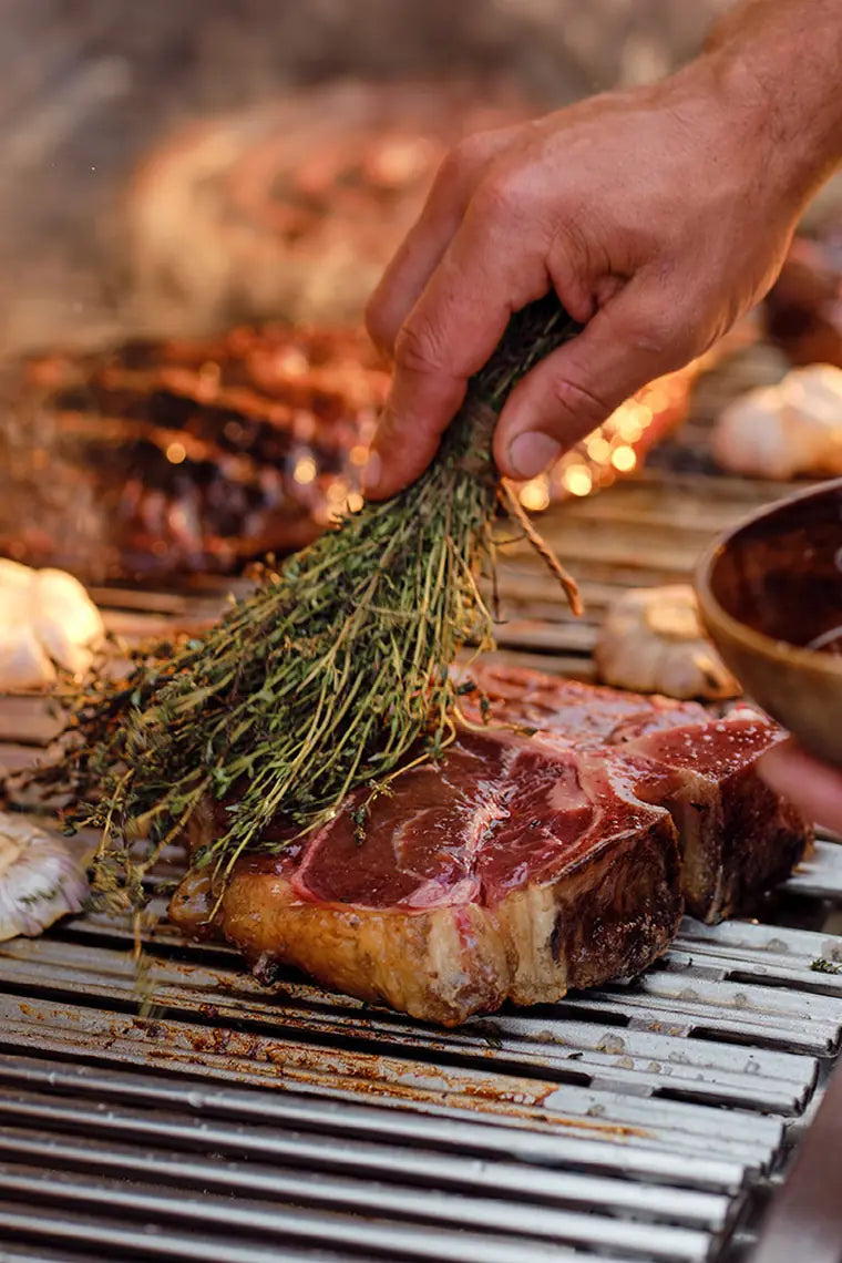 grilling a t-bone steak and brushing with a bunch of rosemary