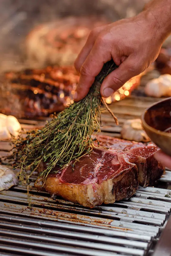 grilling a t-bone steak and brushing with a bunch of rosemary