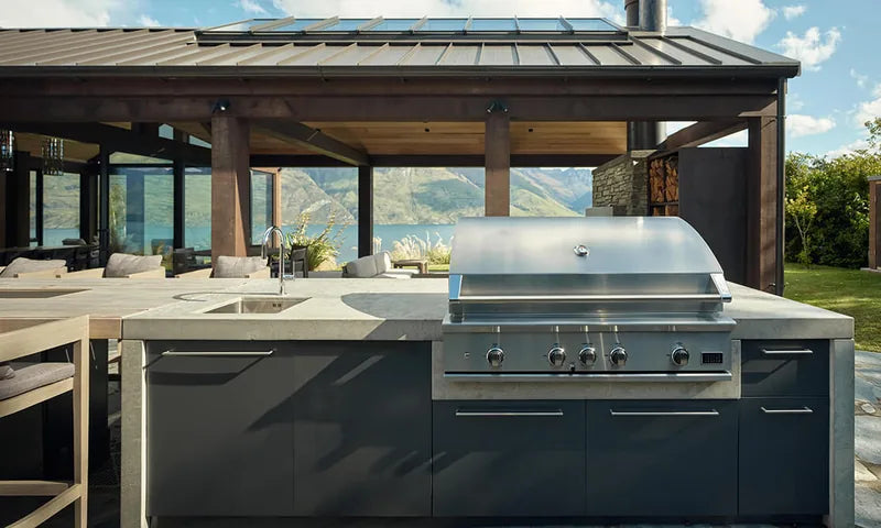 Stainless steel built-in gas grill integrated into a modern outdoor kitchen island with mountain lake views