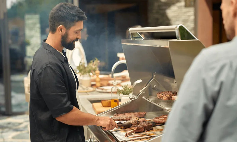 Man grilling steaks on a premium stainless steel Kickass Grill in an outdoor kitchen setting