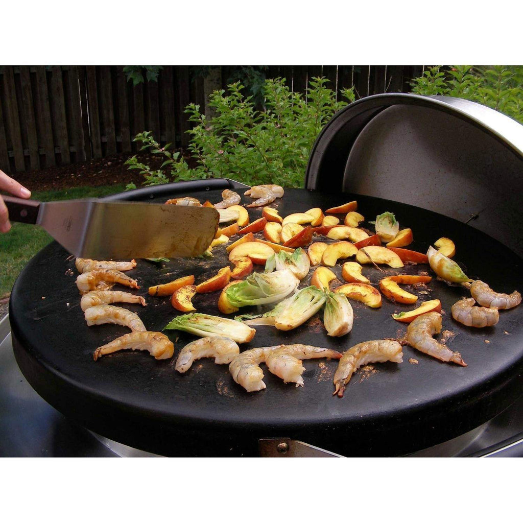 Tabletop gas grill with open black cooking grate and sautéing chicken and vegetables